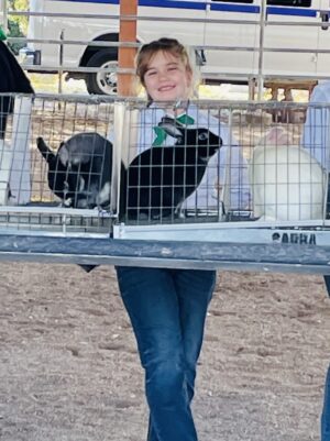 Girl holding two rabbits in a cage.